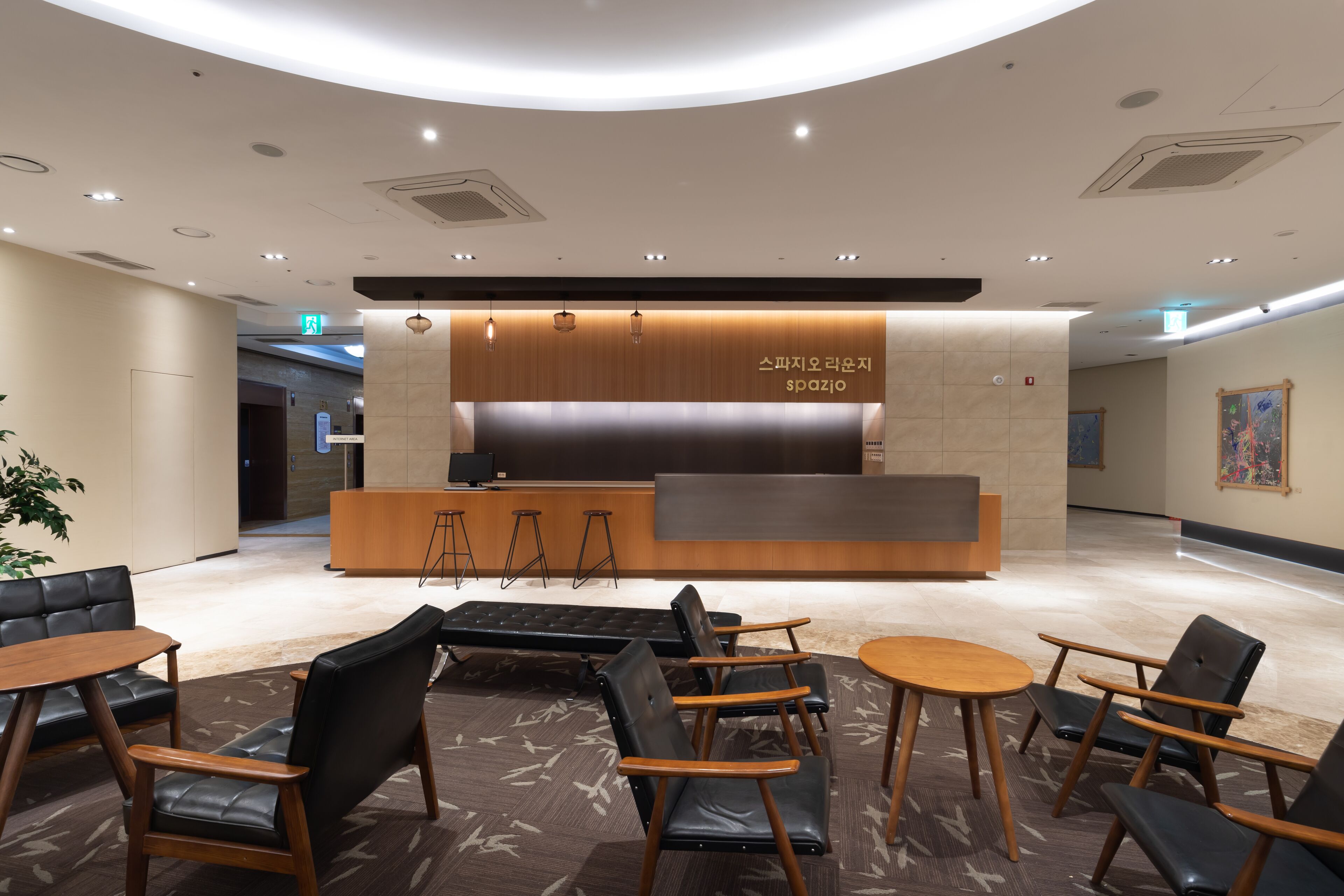 A modern reception area with a wooden counter, black leather seating, and a patterned carpet.