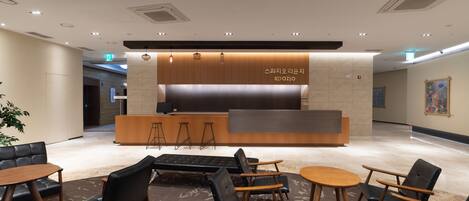 A modern reception area with a wooden counter, black leather seating, and a patterned carpet.