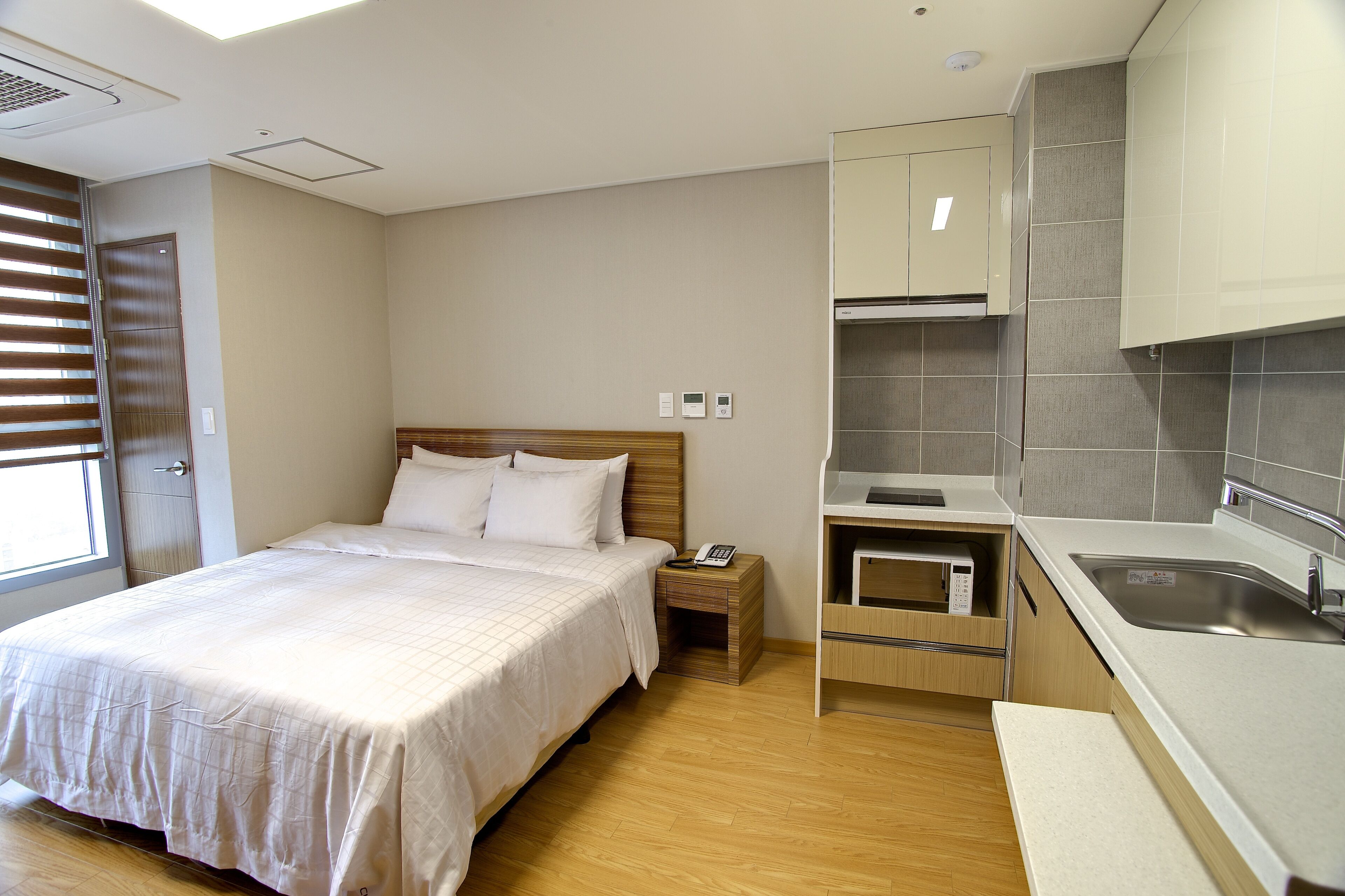 A hotel room with a bed, bedside table, and a built-in kitchen area.