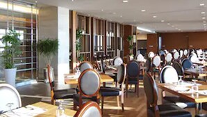 A modern dining area with multiple tables and chairs, large windows, and indoor plants. - The Class 300 (Sokcho)