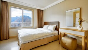 Quarto de hotel com uma cama, escrivaninha de madeira, espelho e vista para montanhas pela janela.