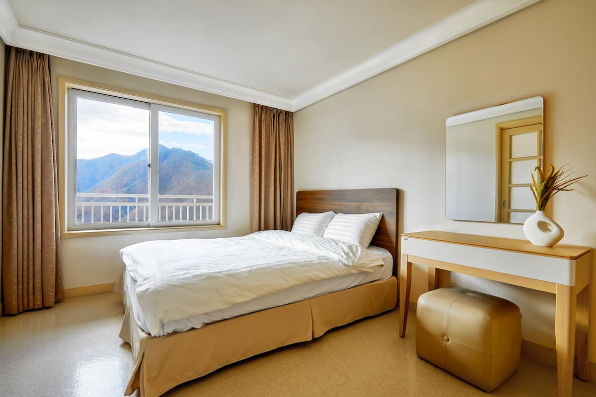 Une chambre d’hôtel avec un lit, un bureau en bois, un miroir et une vue sur les montagnes par la fenêtre.