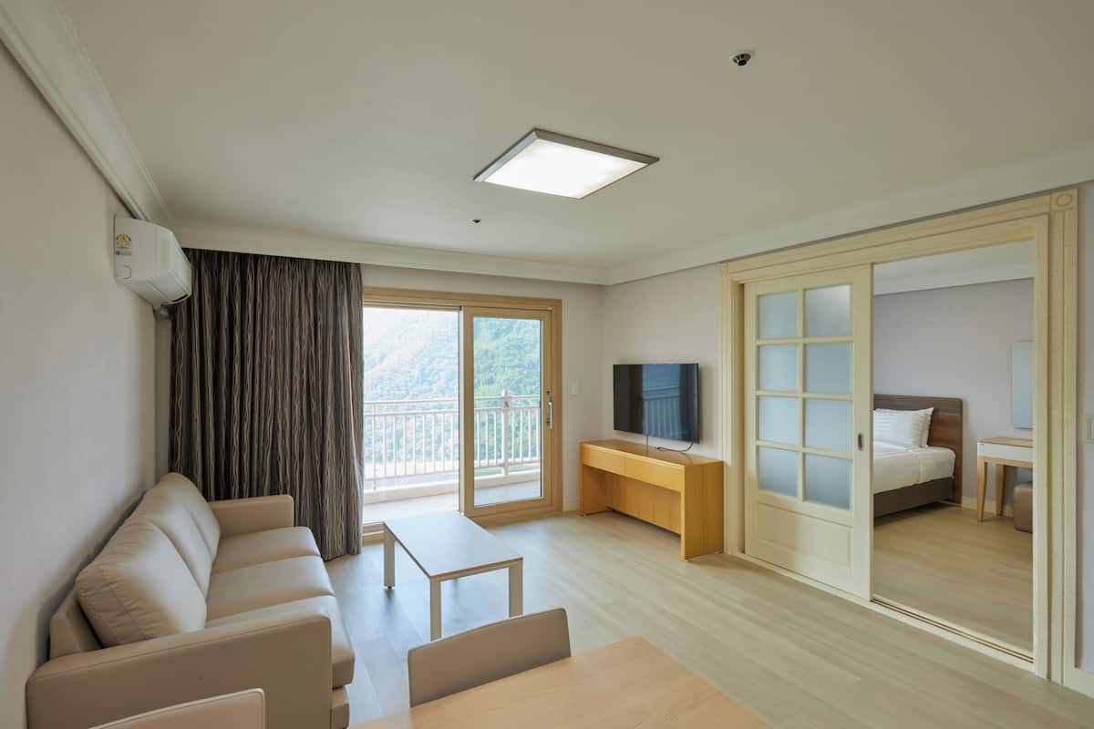 Une chambre d’hôtel moderne équipée d’un canapé, d’une petite table, d’un téléviseur, d’une porte coulissante donnant sur un balcon et d’un bureau en bois.