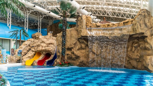 Um parque aquático interno com uma piscina grande, toboáguas e uma cascata.