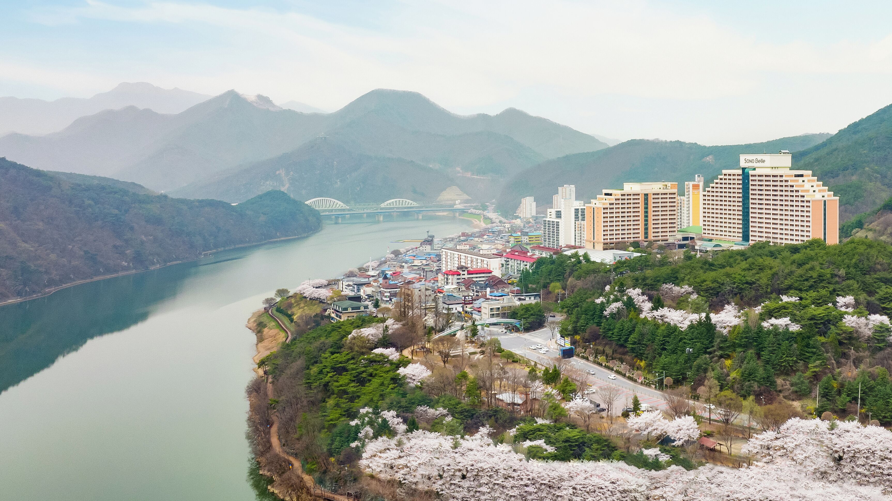 A coastal cityscape with a river, mountains, and a bridge.