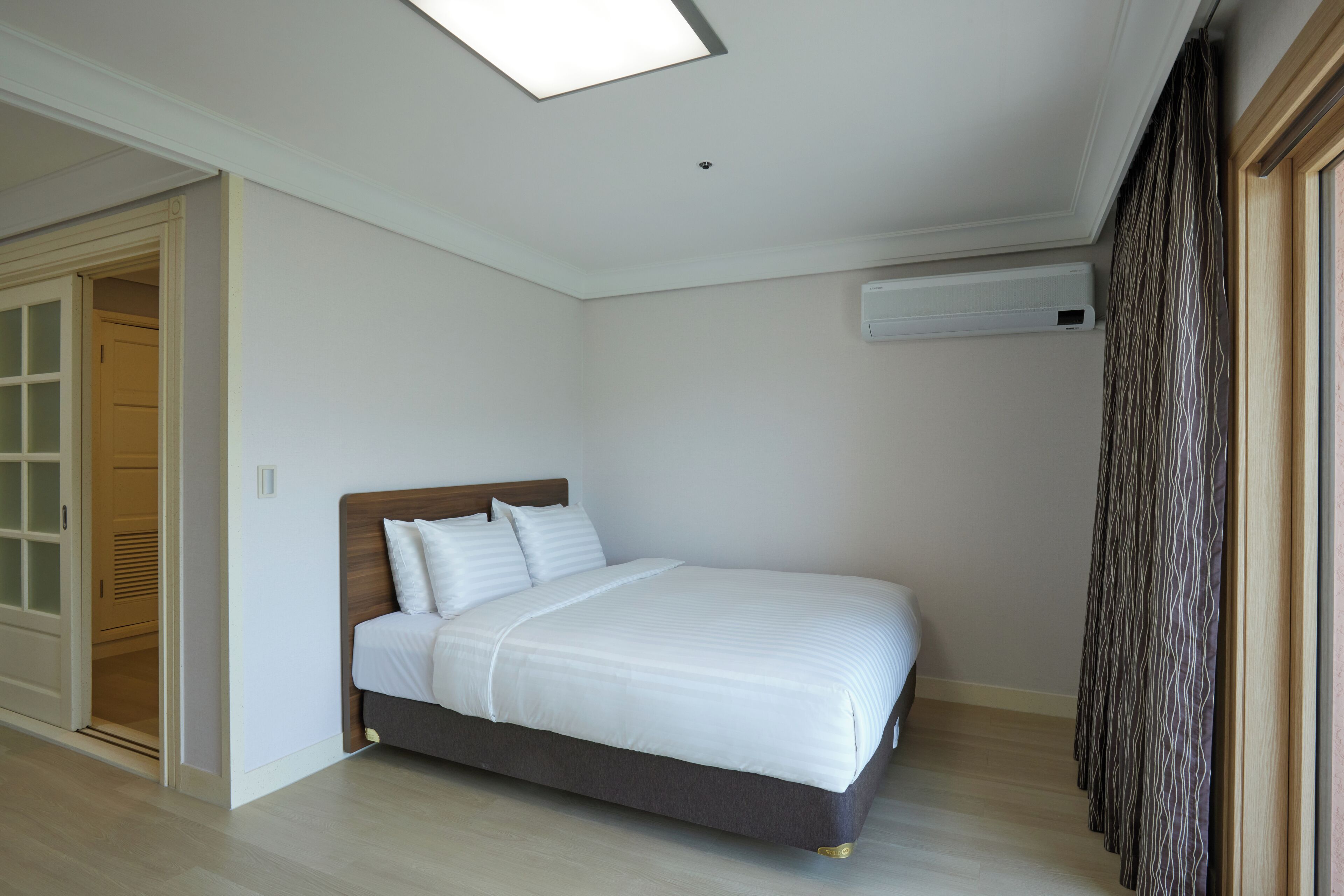 Quarto com cama, luminária no teto, guarda-roupa e aparelho de ar condicionado.