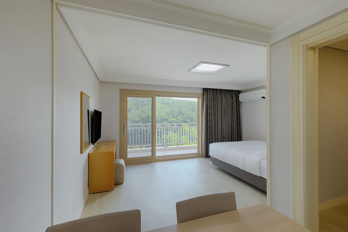 Une chambre d’hôtel comprenant un lit, un bureau, une chaise, une télévision et un balcon avec vue sur la verdure.