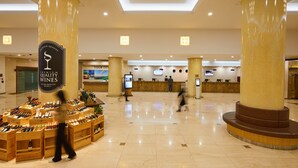 Um saguão de hotel com exposição de vinhos, balcão de recepção e grandes colunas.
