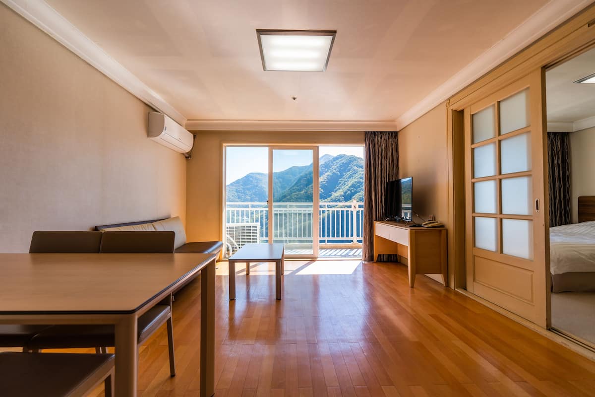 Une chambre d’hôtel avec un plancher en bois, un balcon offrant une vue sur les montagnes, un bureau avec une télévision et un lit.