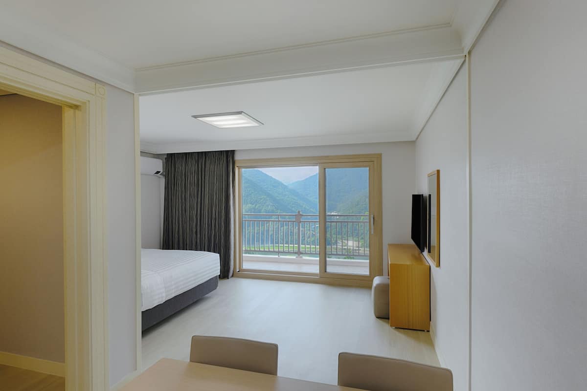 Une chambre d’hôtel équipée d’un lit, d’un bureau, d’une chaise, d’une télévision et d’un balcon avec vue sur la montagne.
