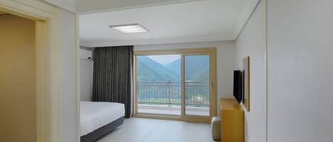A hotel room with a bed, a desk, a chair, a TV, and a balcony with a mountain view.