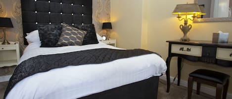 A hotel room with a large bed, a desk with a lamp, a chair, and a mirror on the wall.