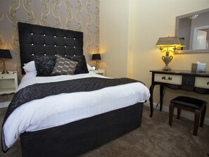 Een hotelkamer met een groot bed, een bureau met lamp, een stoel en een spiegel aan de muur.