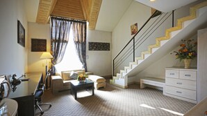 A hotel room with a staircase, a desk with a chair, a sofa, a coffee table with flowers, and a dresser. - Metro Tourist Hotel (Cheonan)