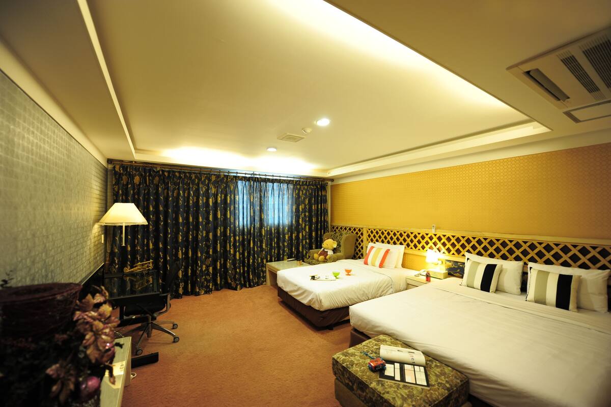 Une chambre d’hôtel avec deux lits, un bureau, une chaise, une lampe et une petite table.