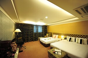 Habitación de hotel con dos camas, un escritorio con lámpara, una silla y una mesita con control remoto.