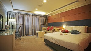A hotel room with a large bed, a desk, a chair, a small table, and a TV. - Metro Tourist Hotel (Cheonan)