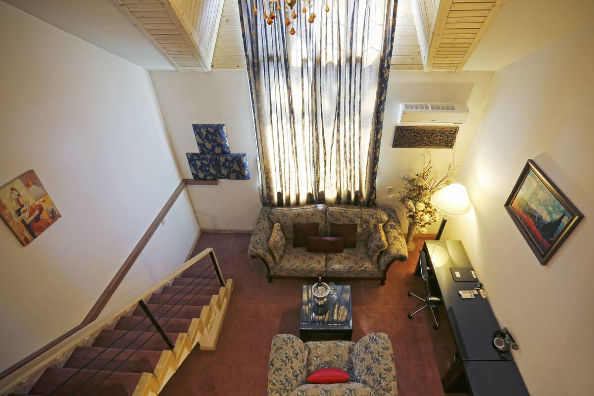 Un salon comprenant un canapé, une table basse et un bureau. Un escalier avec une rampe mène à un autre niveau.