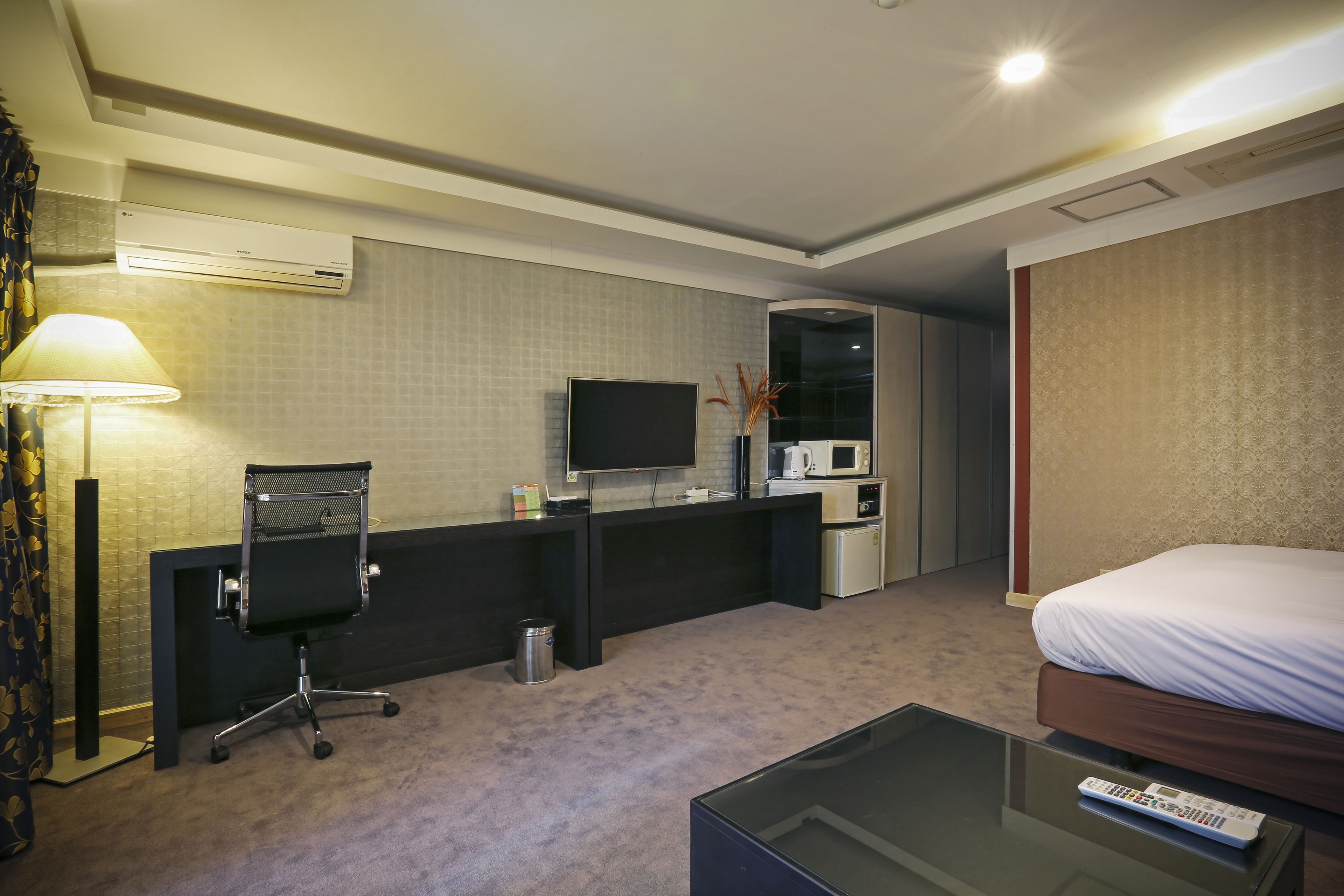 Hotelkamer met een bed, een bureau met een stoel, een televisie, een magnetron en een afstandsbediening op een glazen tafel.