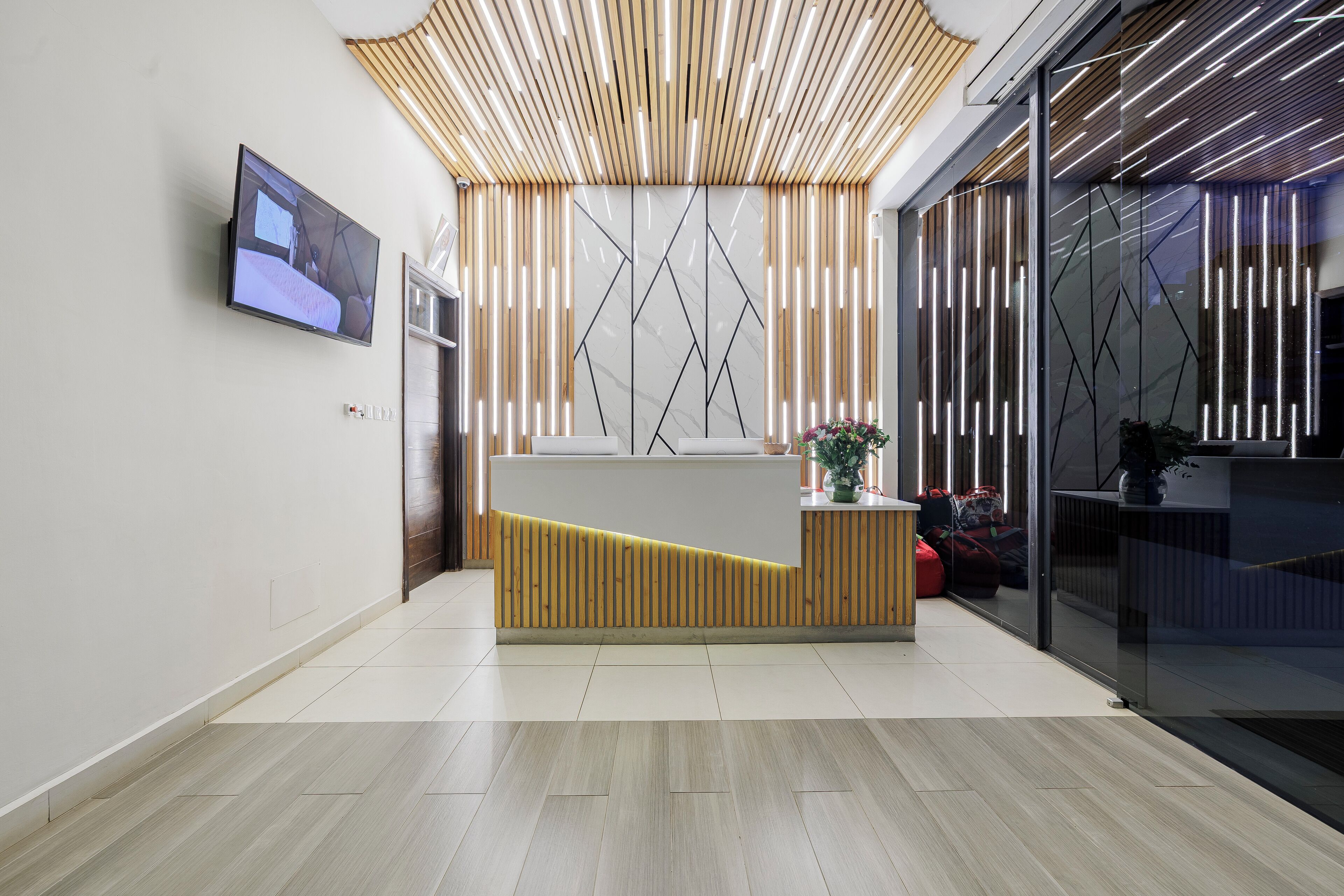 A modern reception area with a wooden reception desk, a flat-screen TV, and a glass partition.