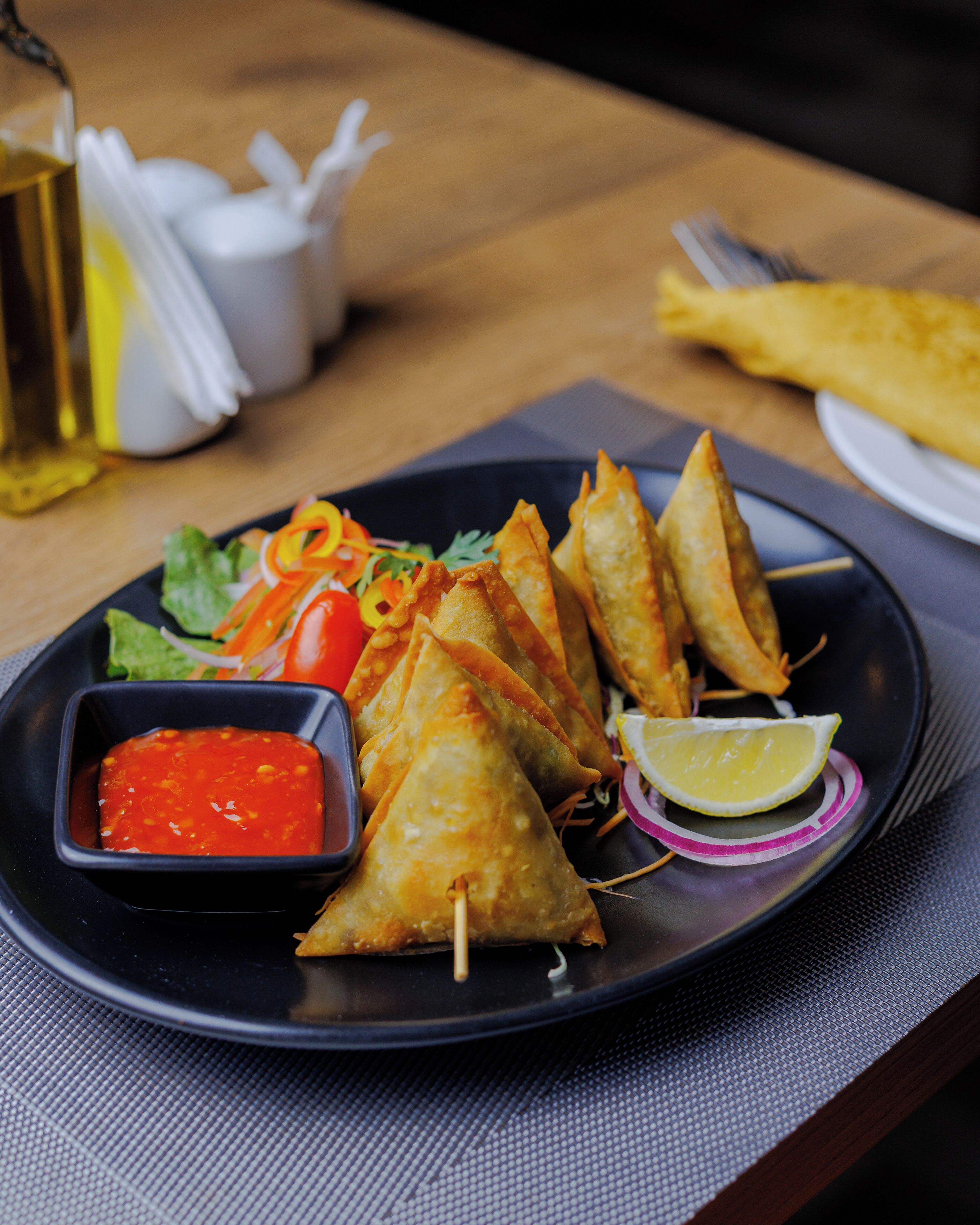 A plate of samosas with a side of dipping sauce and lemon slices.