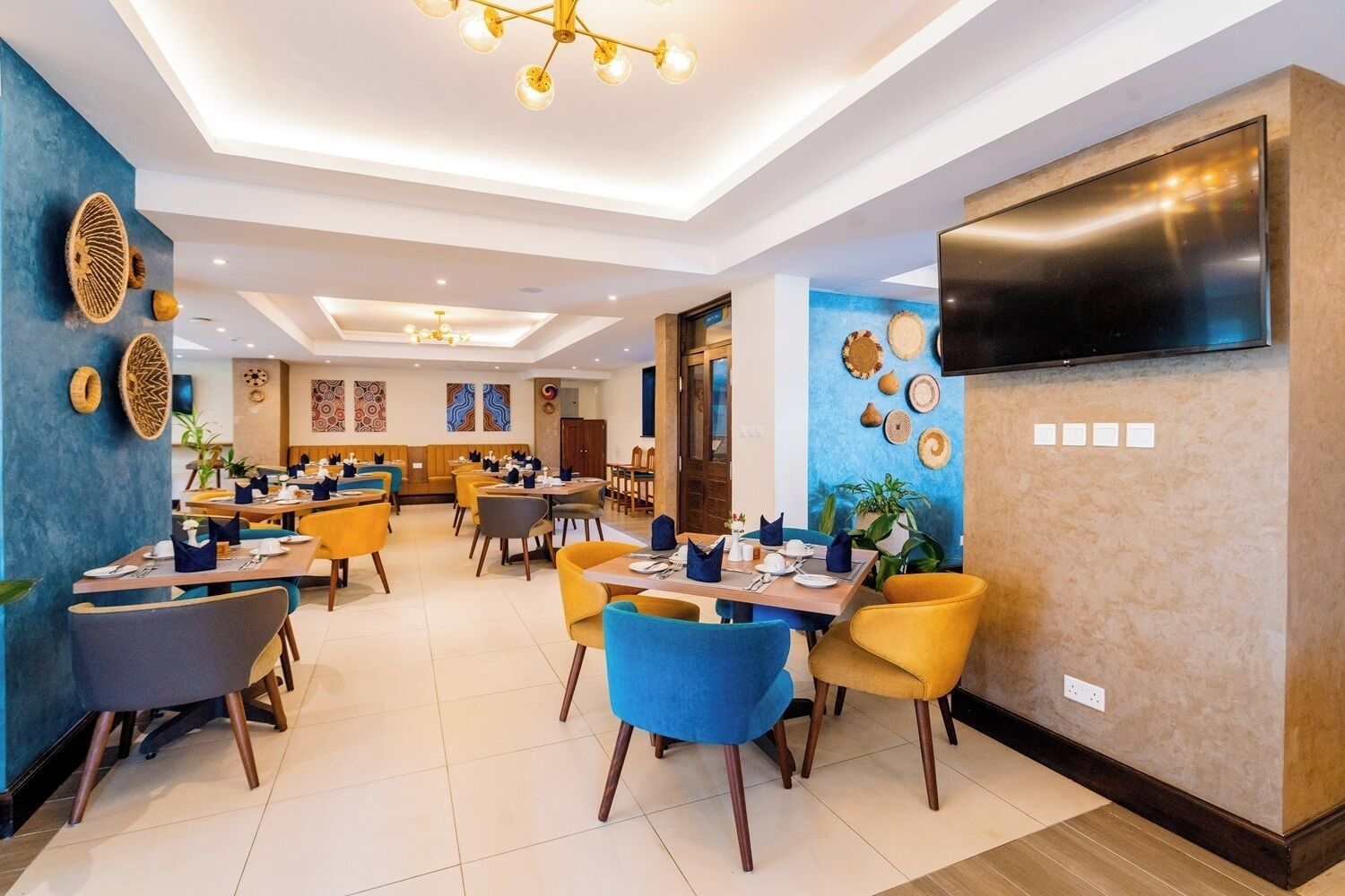 A modern dining area with multiple tables and chairs, a flat-screen TV mounted on the wall, and decorative wall art.