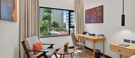 Une chambre d’hôtel équipée d’un bureau, de deux chaises, d’un lit, d’une petite table agrémentée de fleurs et offrant une vue sur les bâtiments environnants.