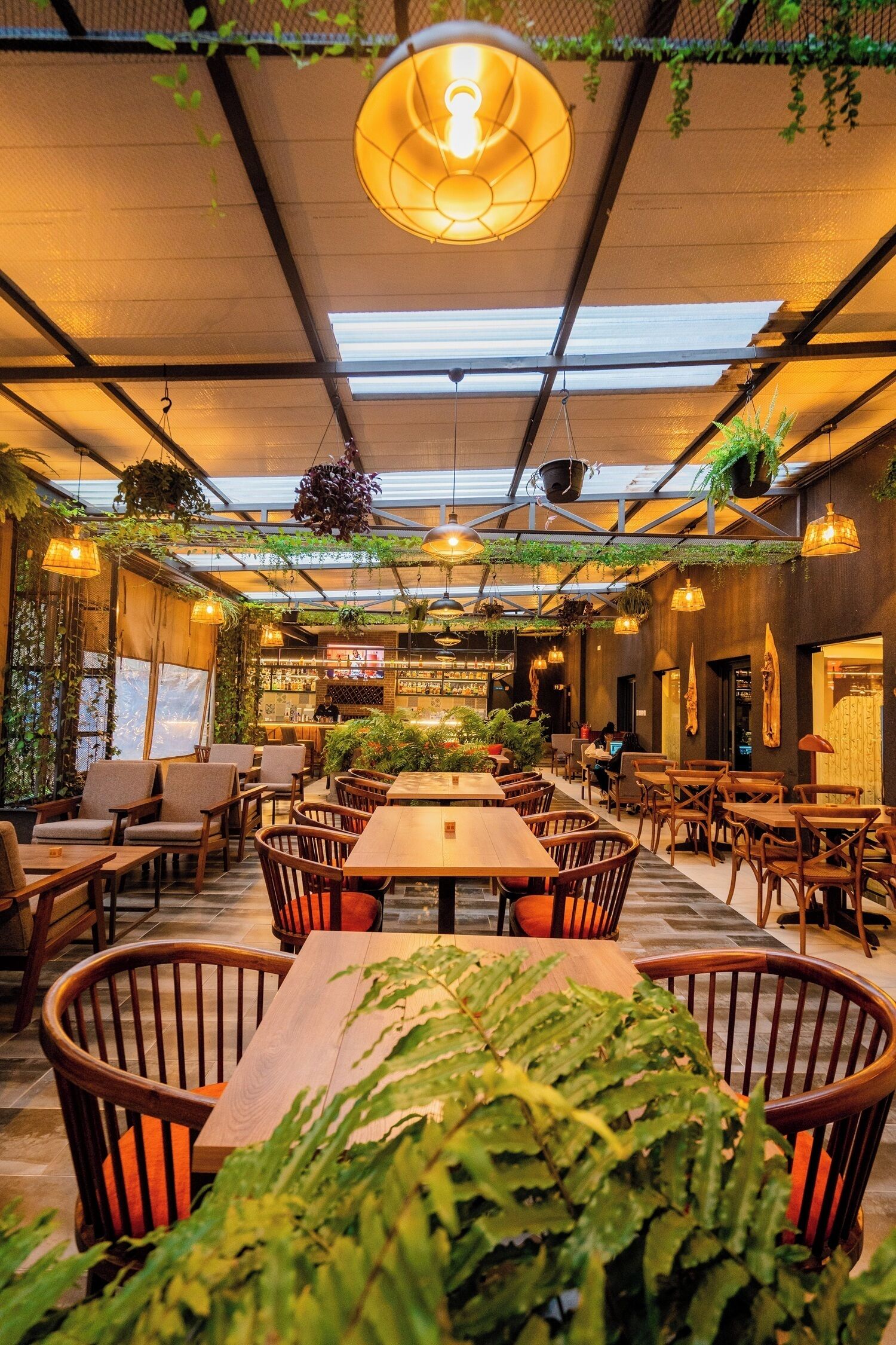 Un espace de restauration intérieur avec des tables et des chaises en bois, des plantes suspendues et un luminaire central.