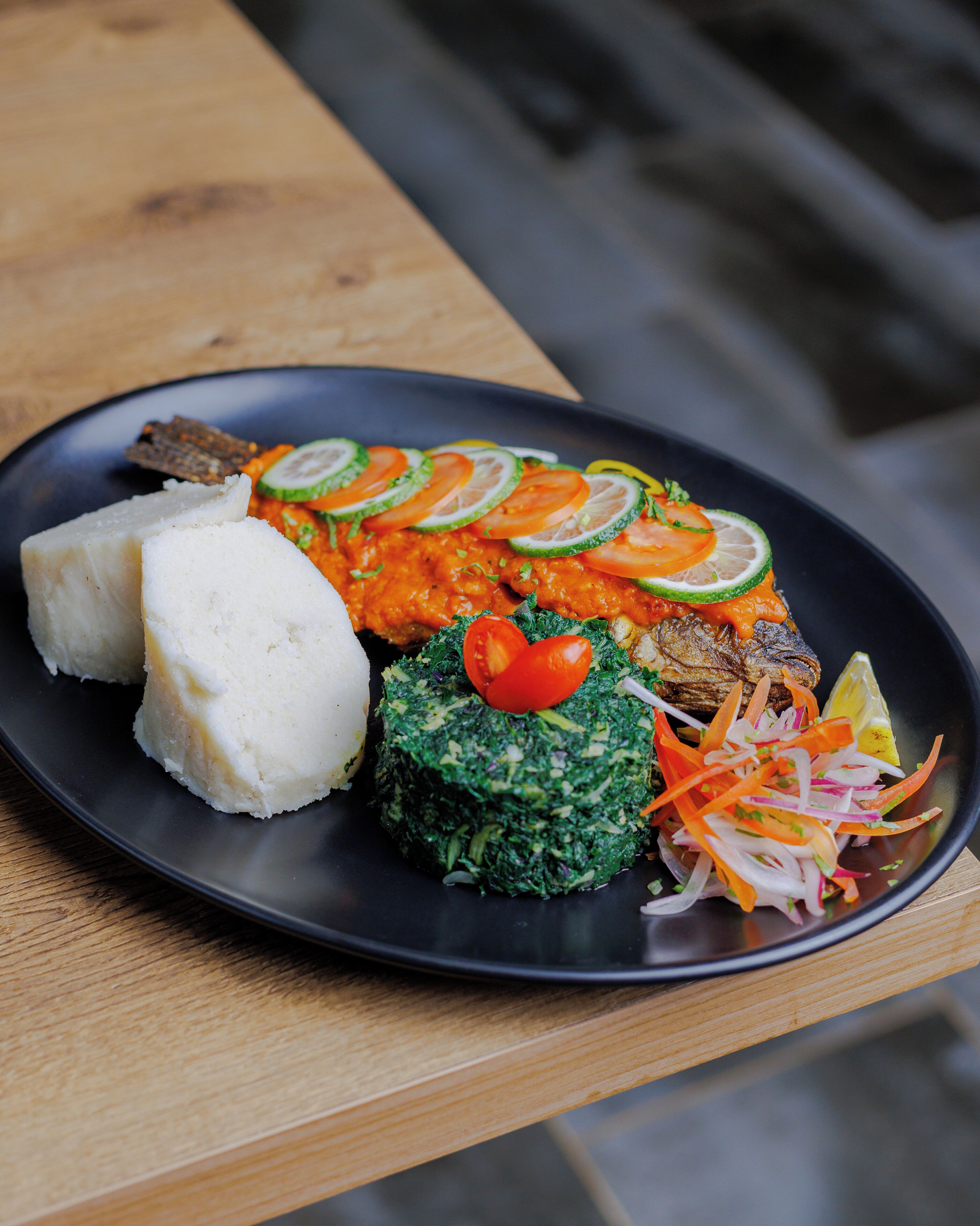 A plate of food with various dishes including a grilled fish, a green vegetable patty, a white food item, and a salad.