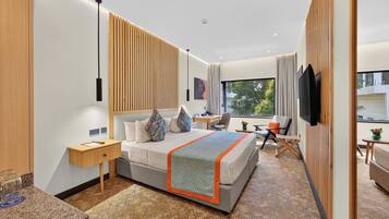 Una habitación de hotel moderna con una cama grande, un escritorio, una silla, un televisor y una ventana con vistas.