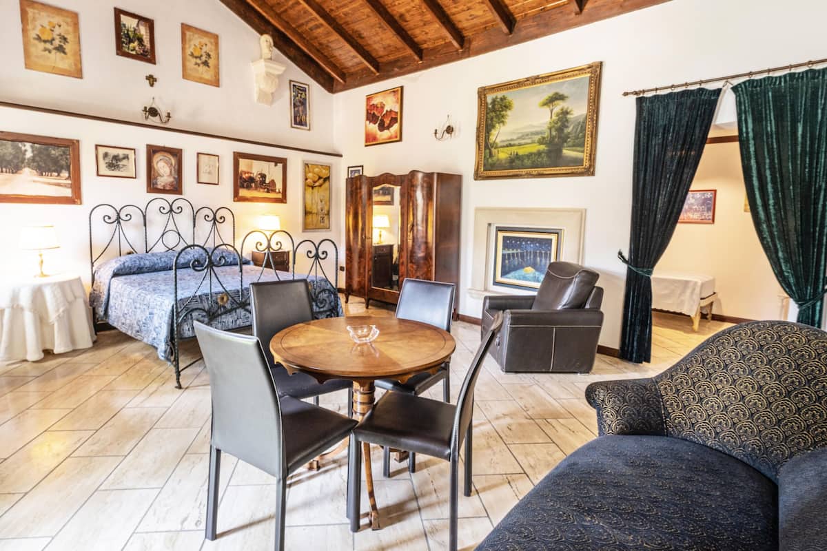 A room with a bed, a dining table with chairs, a sofa, and a fireplace.