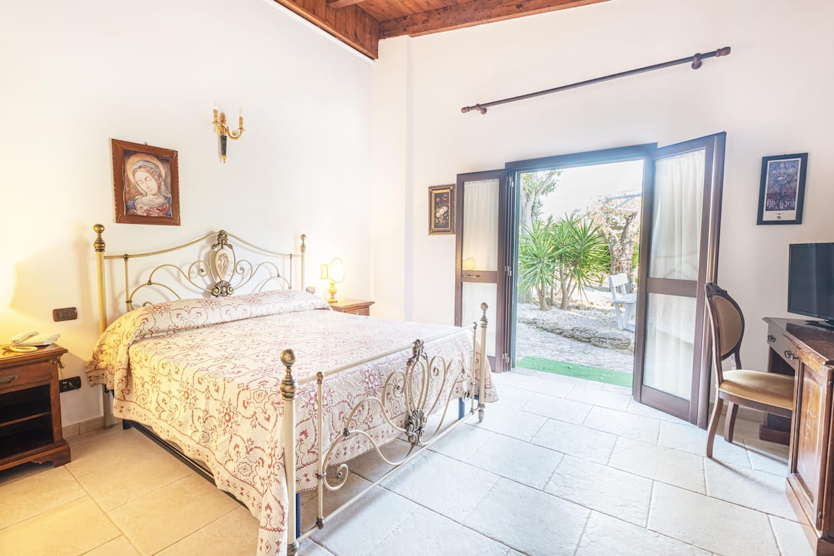 A bedroom with a bed, bedside table, lamp, and a view of the outdoors through a sliding door.