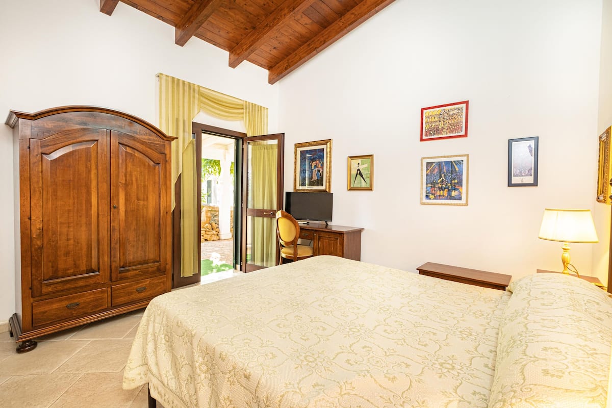 A bedroom with a large bed, wooden wardrobe, and a television on a cabinet.