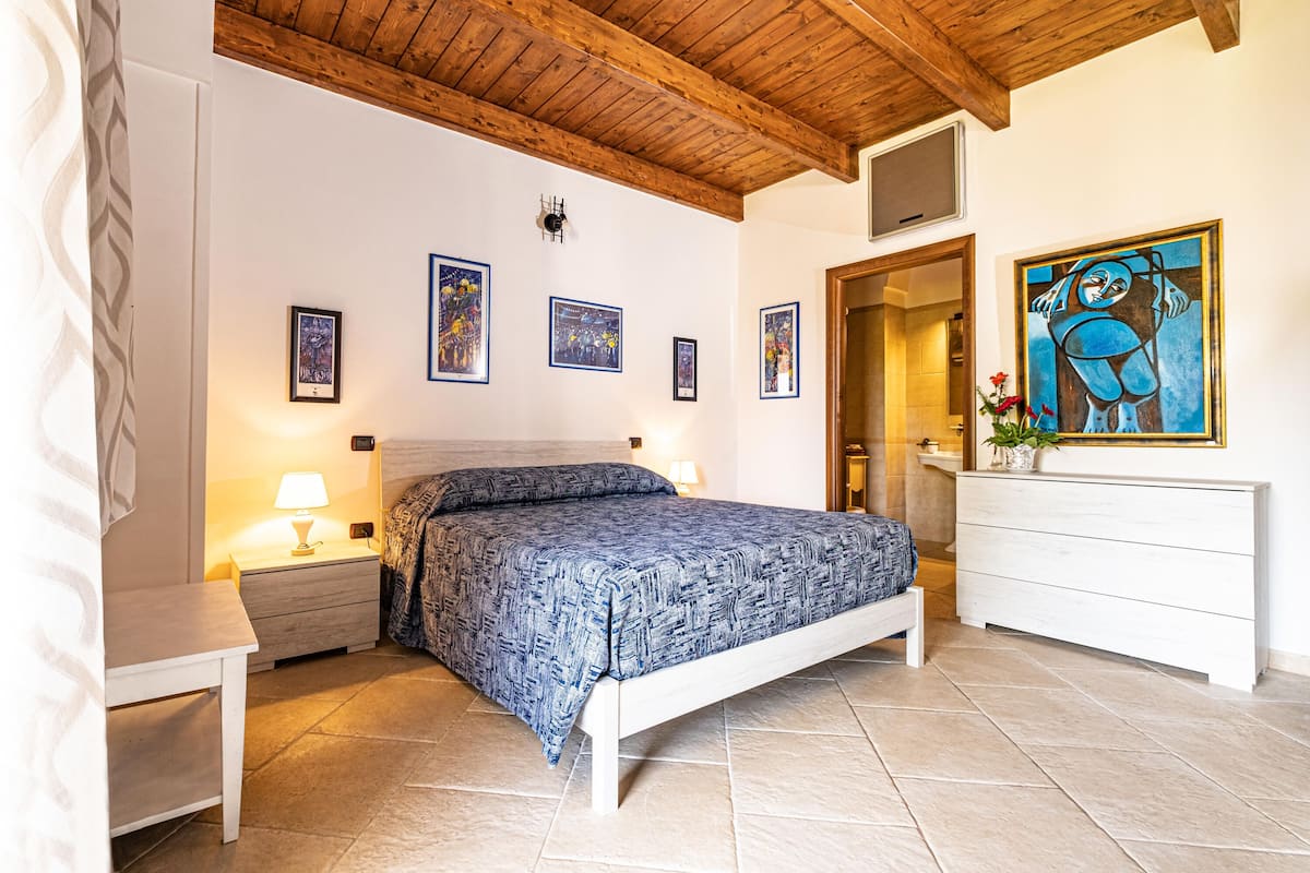 A bedroom with a bed, bedside tables, a dresser, and artwork on the walls.