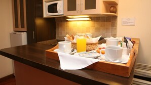 Bandeja de desayuno con cruasanes, jugo de naranja y tazas de café sobre una encimera de madera en una cocina de hotel.