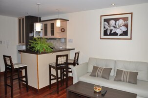 A modern living room with a sofa, a coffee table, and a dining area with chairs and a small island.