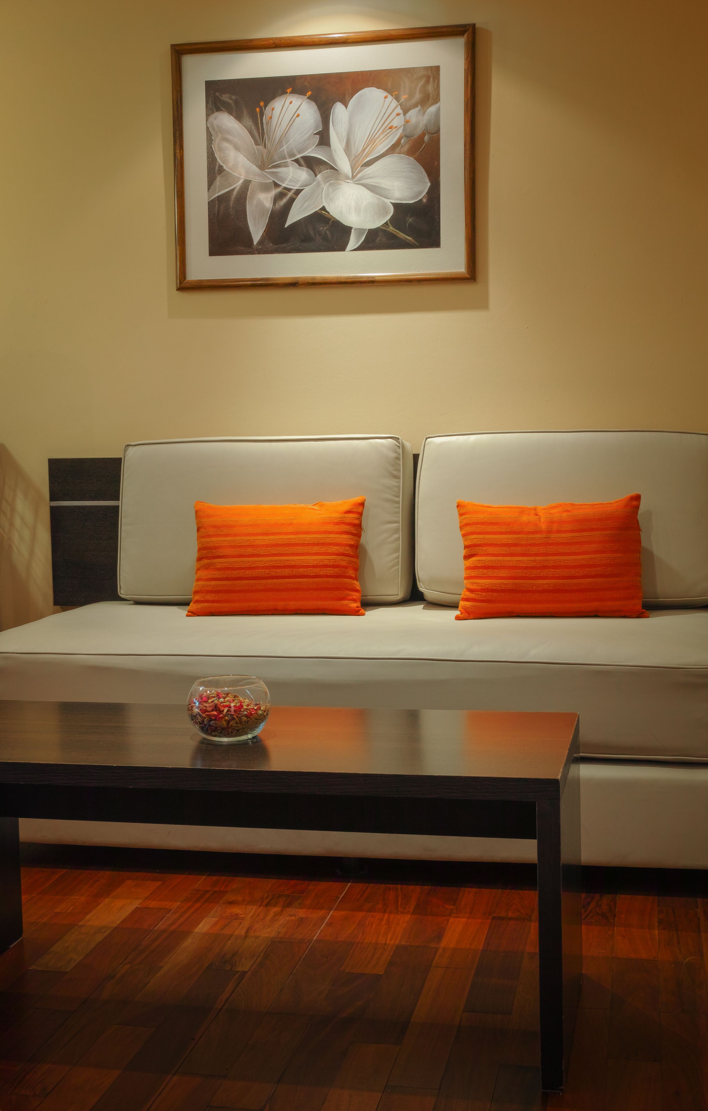 Una habitación con un sofá, dos almohadas naranjas, un cuadro en la pared y una mesa de centro con un bol de caramelos.
