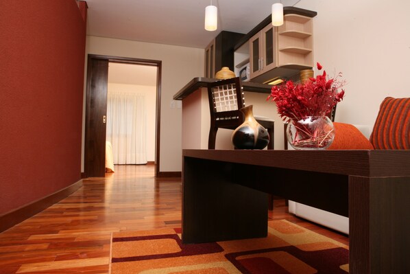 Una sala moderna con una mesa de centro de madera, un jarrón con flores rojas y un cojín a rayas.