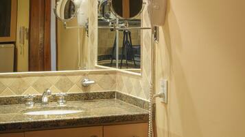 A bathroom with a sink, mirror, hairdryer, and towel rack.