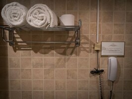 Un baño con un perchero que sostiene toallas enrolladas y un secamanos. Se ve un cartel en la pared.