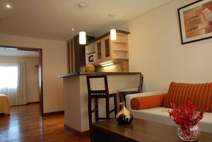 Una sala de estar moderna con sofá, una mesita de centro y una zona de cocina con armarios y lámparas colgantes.
