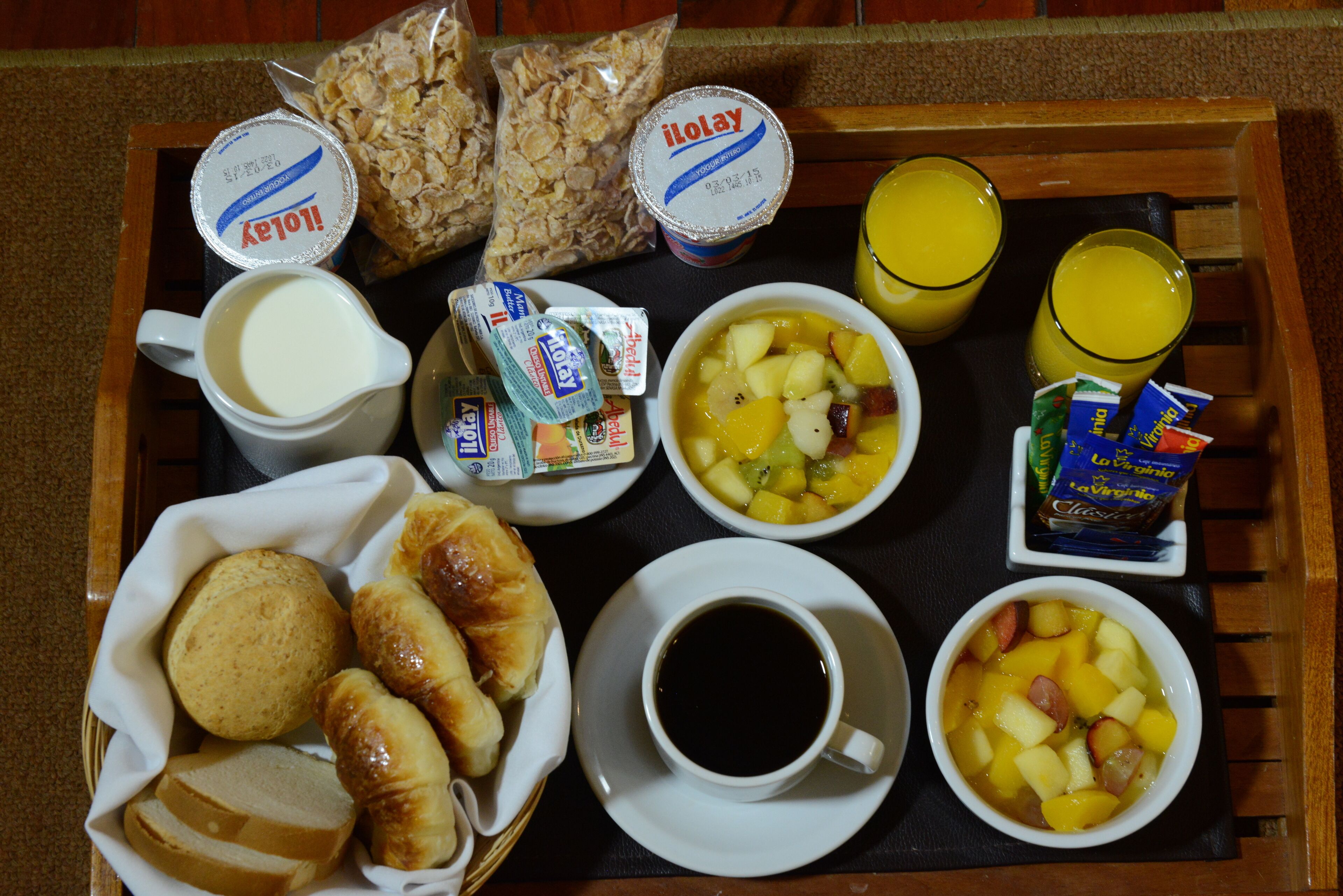 Bandeja de desayuno con croissants, cereales, fruta, jugo, café y yogur.