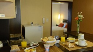 Desayuno con una taza de café, jugo, cereal y pastelería sobre una mesa en una habitación de hotel.