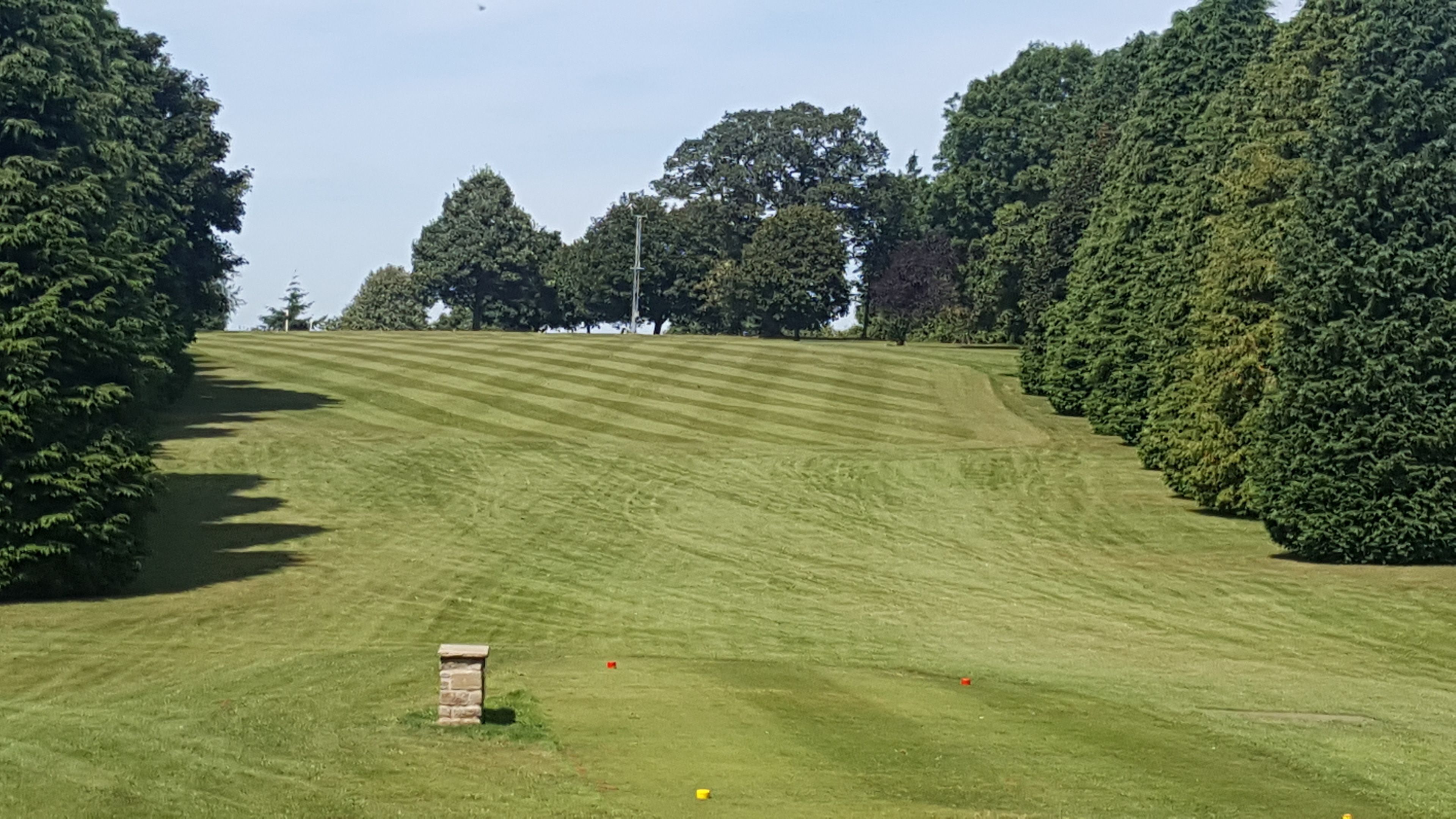 A golf course with a well-maintained lawn, a stone structure, and trees in the background.