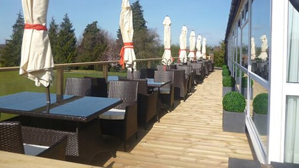 An outdoor patio with tables and chairs, umbrellas, and a wooden deck.