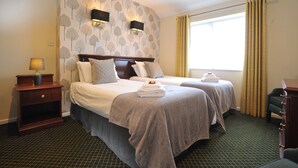 A hotel room with two beds, a nightstand with a lamp, a dresser, and a window with curtains.