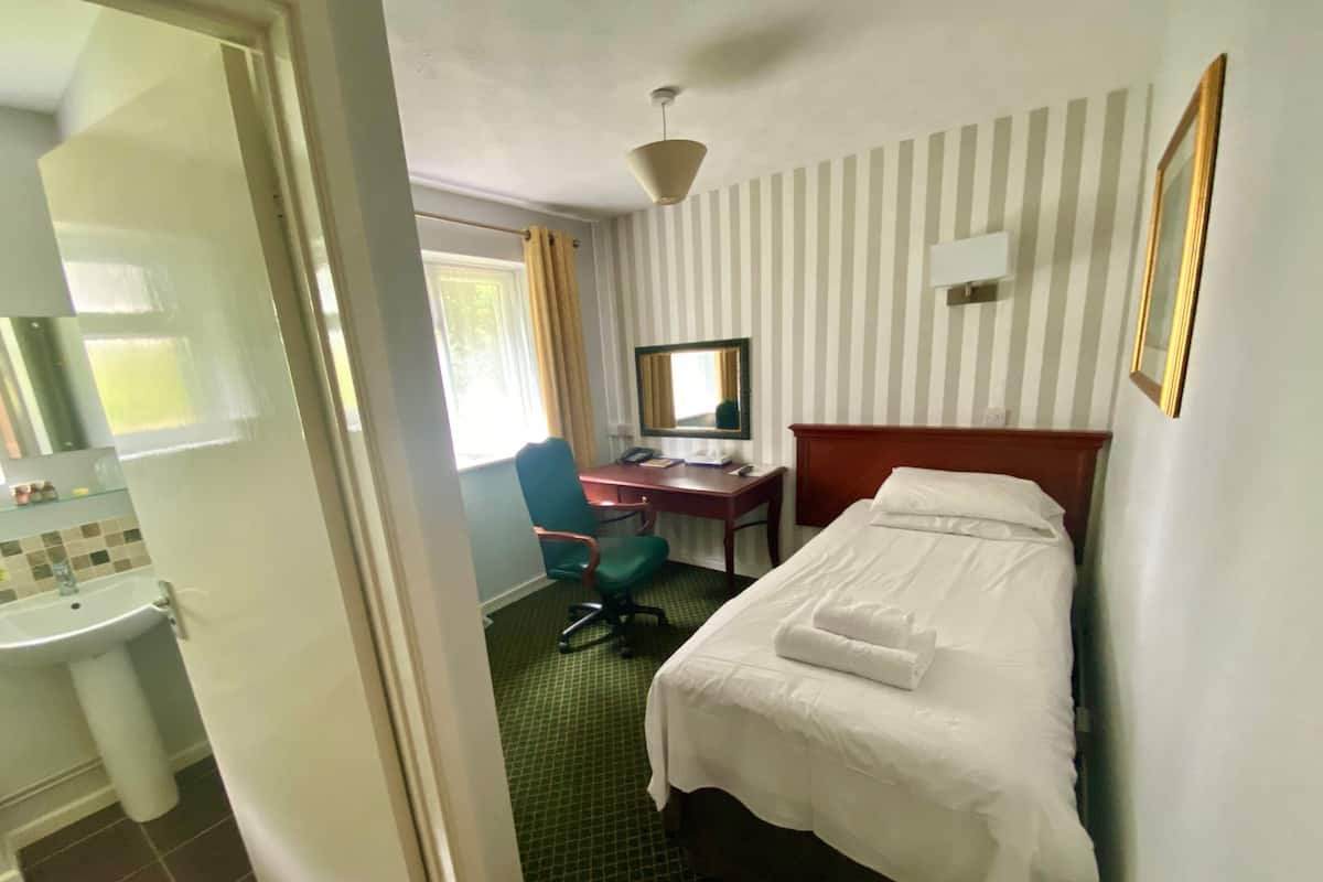 Hotellihuone, jossa on sänky, työpöytä, tuoli, pesuallas ja ikkuna, jossa on verhot.