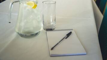 A conference room with a long table, chairs, a projector screen, a pitcher, a glass, and a notepad.