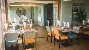 A dining area with multiple tables and chairs, a round mirror on the wall, and a wooden floor.
