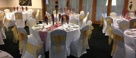 A banquet hall with round tables set for a formal event, each with white tablecloths and gold sashes on chairs.